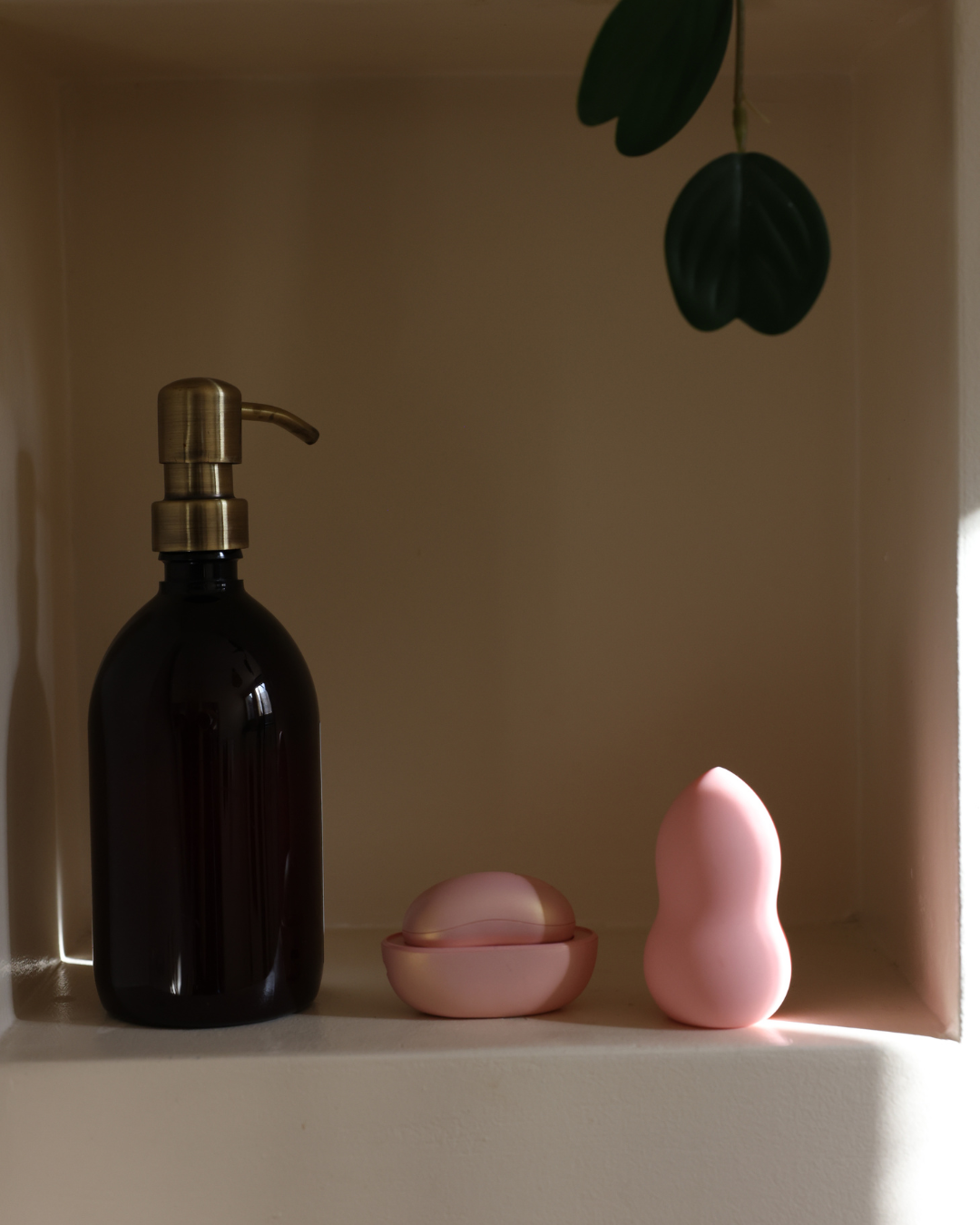Black bottle with gold pump, pink ceramic bowls, and green leaves on a neutral background