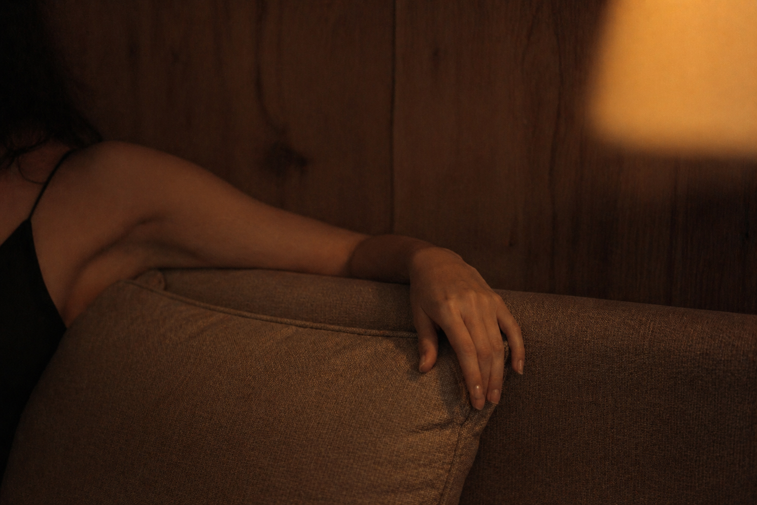 Person sitting on a brown couch with a warm light source in the background