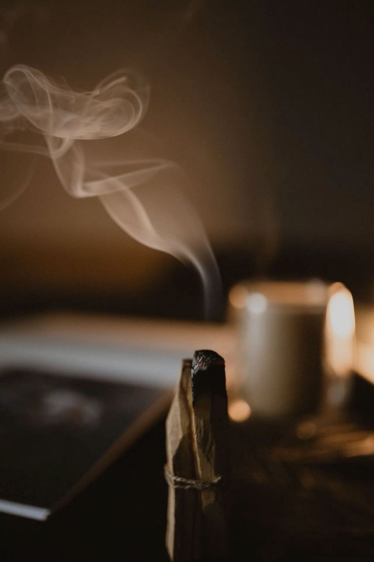 Incense stick with smoke and a blurred candle in the background