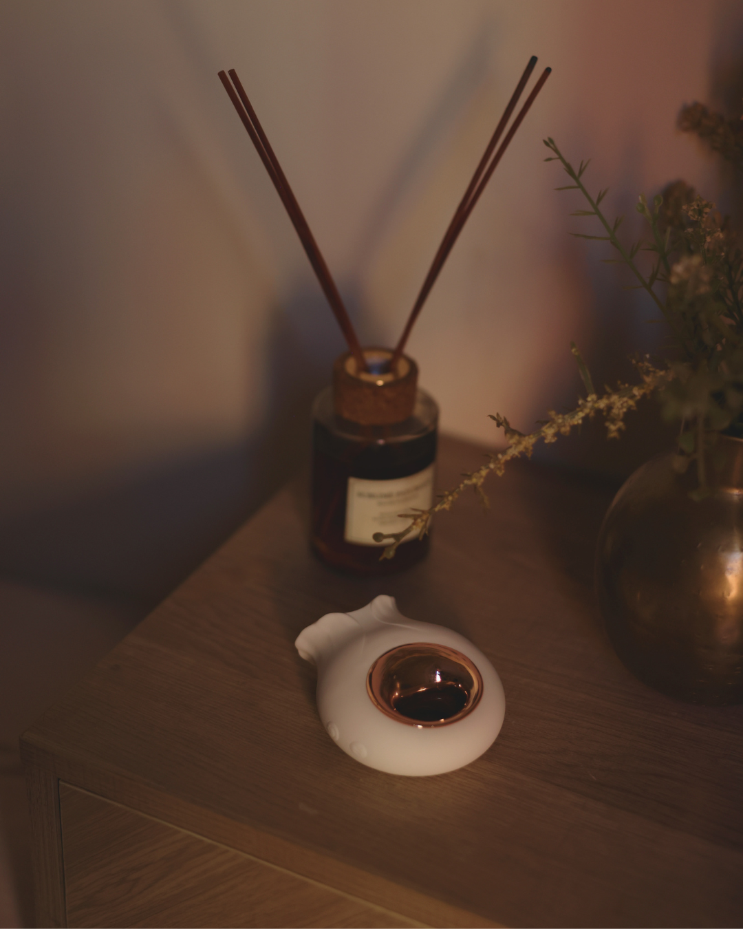 A diffuser with reeds and a small white container on a wooden surface.
