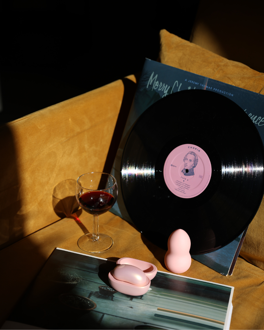 Vinyl record with a pink label on a table with a glass of red wine and a book.