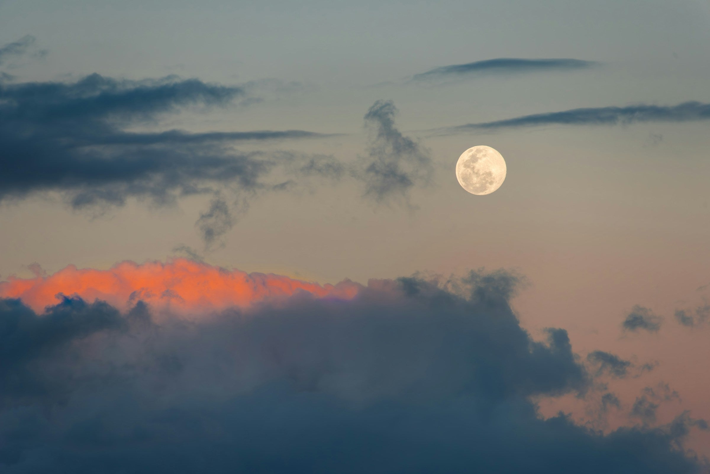 Full moon rising above clouds with a pinkish-orange hue